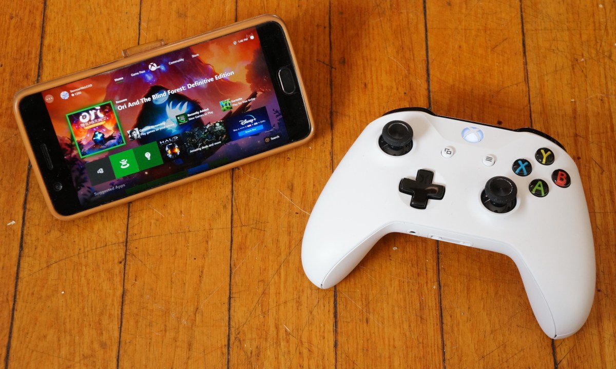 The Xbox Game Pass app on a phone that's displayed on a hardwood floor next to an Xbox controller.