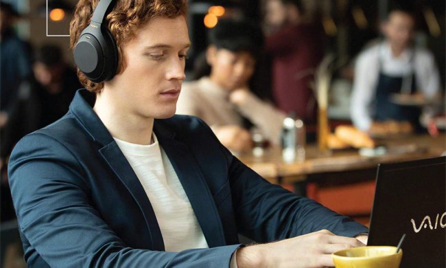 Man in cafe working on a laptop wearing Sony WH1000-XM4 wireless over-the-ear noise-canceling headphones.