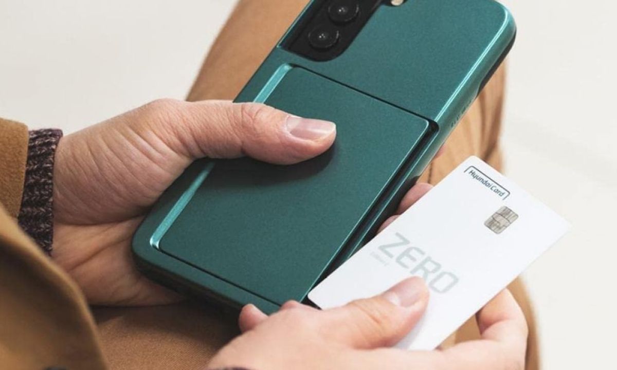 A person holding a card in one hand and the Galaxy S22 in a K-max auto-tok dark green card case in the other.