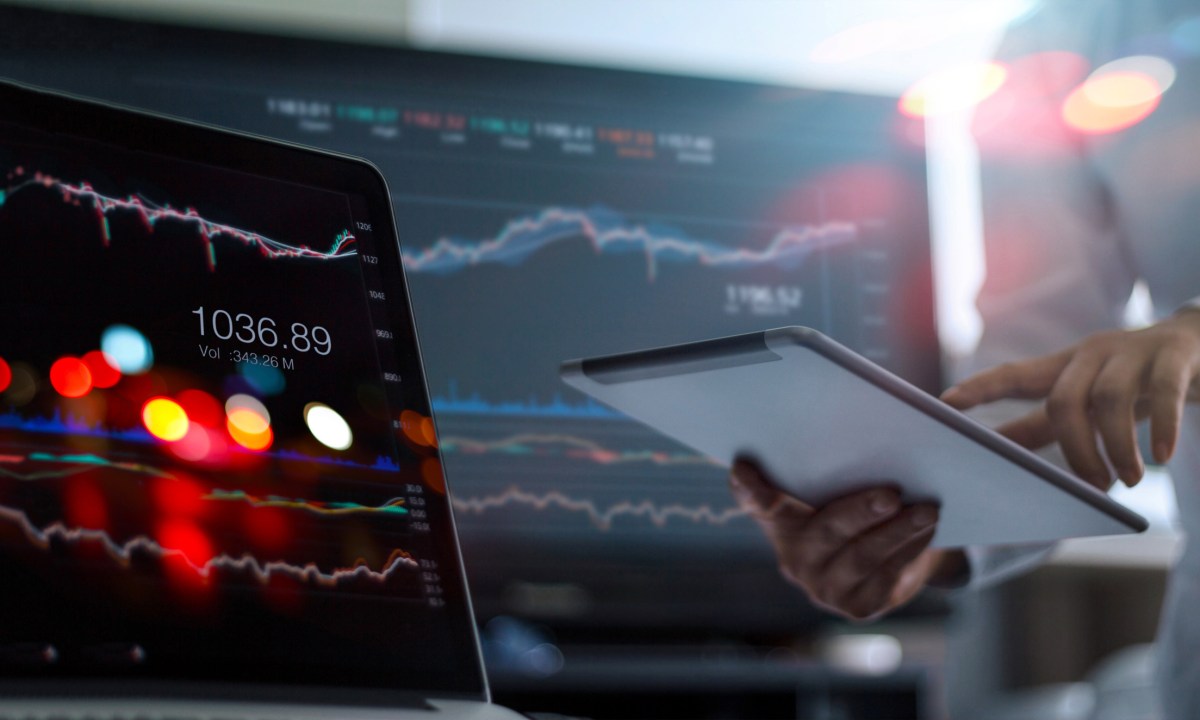 A man using tablet and laptop for analyzing market data.