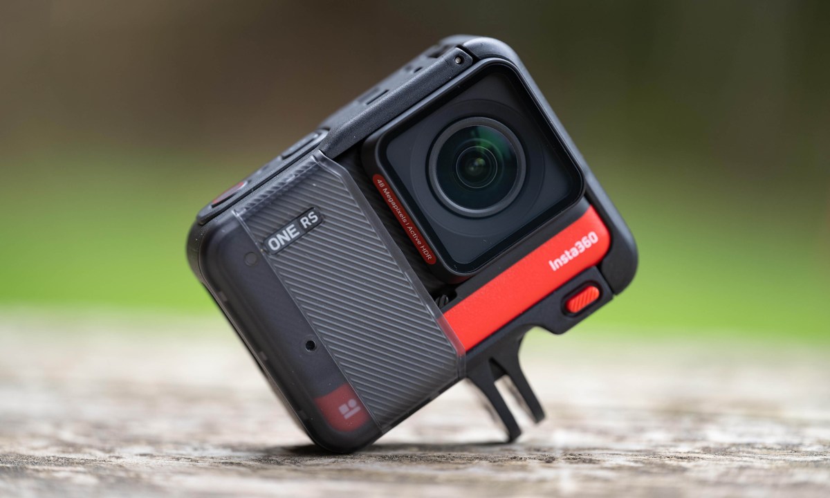 Insta360 One RS on worn wood surface against a green blurred background.