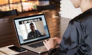 A person conducting a Zoom call on a laptop while sat at a desk.