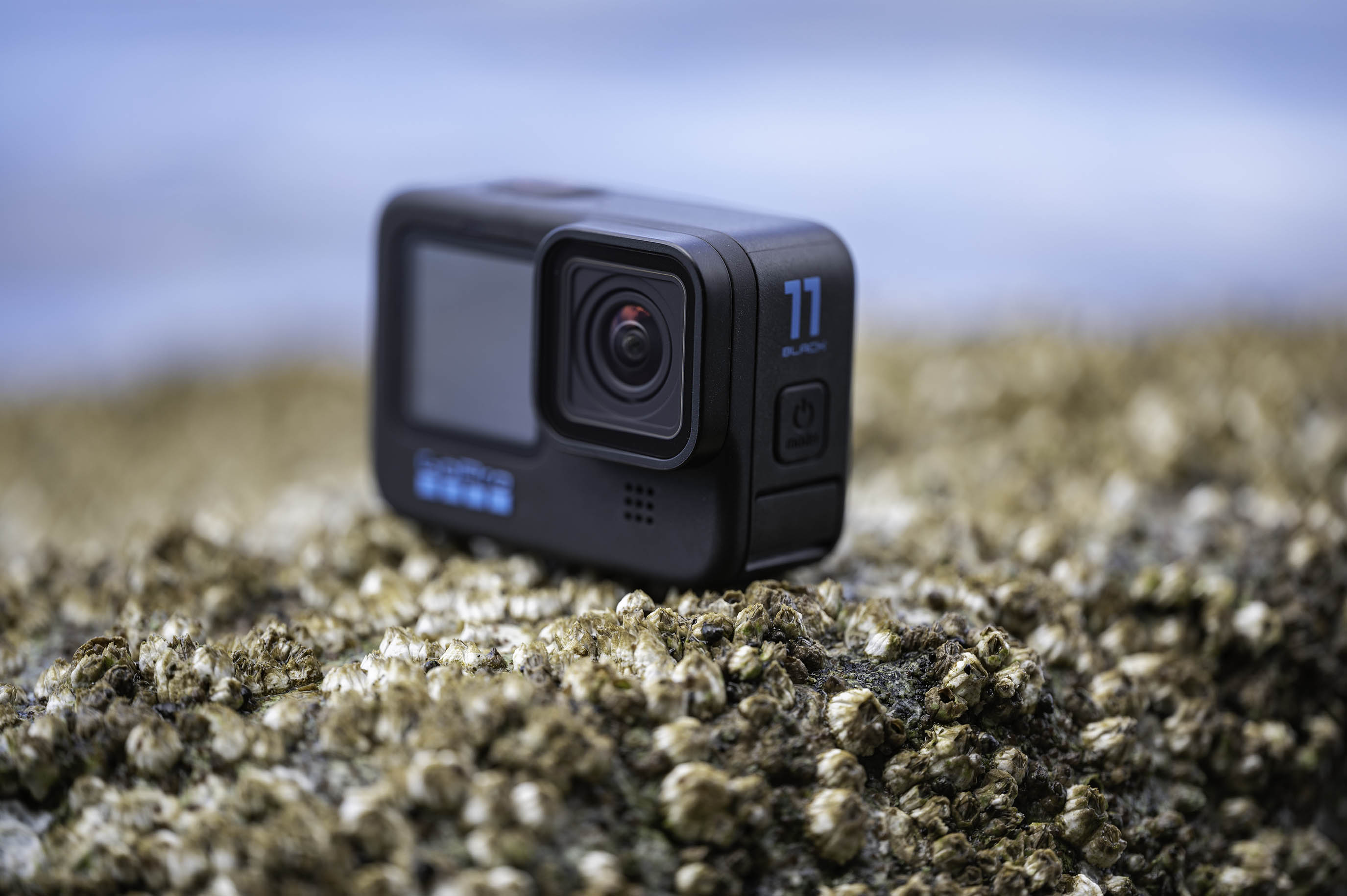 The GoPro Hero 11 Black on a rock with barnacles next to the ocean.