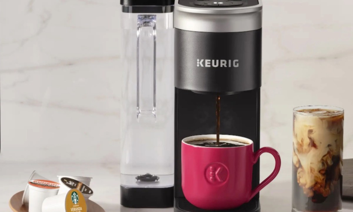 A Keurig K-Supreme coffee maker sits on a kitchen counter next to K-Cups and glass of iced coffee.