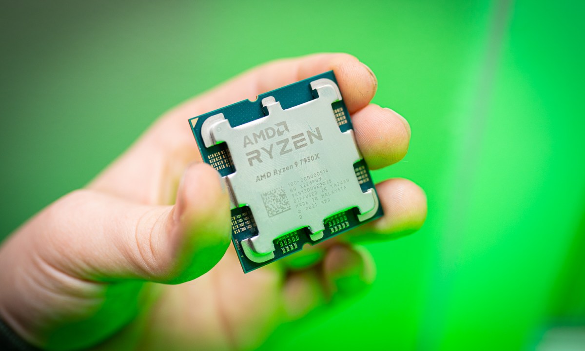 A hand holding the Ryzen 9 7950X in front of a green light.