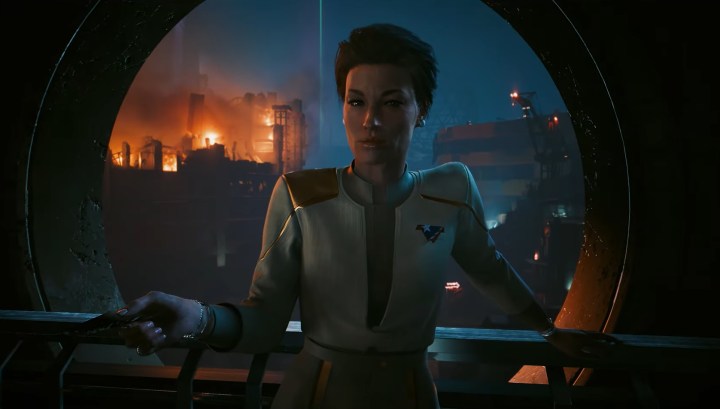Cyberpunk 2077: Phantom Liberty's new character. She's in a security uniform leaning against a railing with a fiery cityscape in the background.