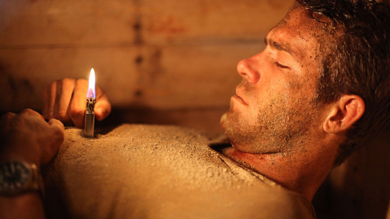 Ryan Reynolds stuck in a coffin underground holding a lighter in a scene from Buried.