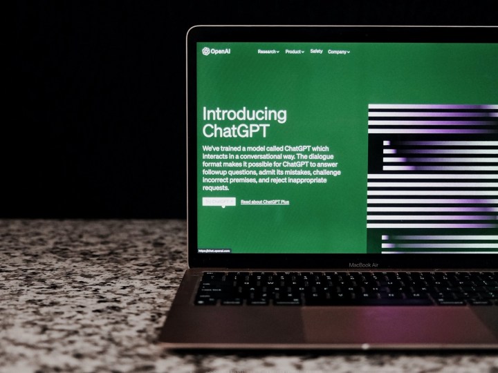 The ChatGPT website on a laptop's screen as the laptop sits on a counter in front of a black background.