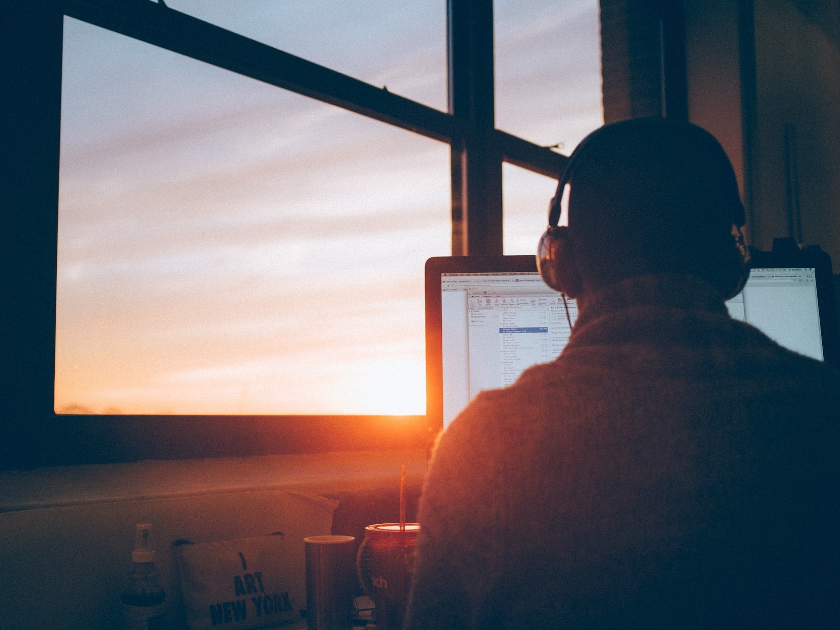 man remote working on laptop from home office with sunset in background.
