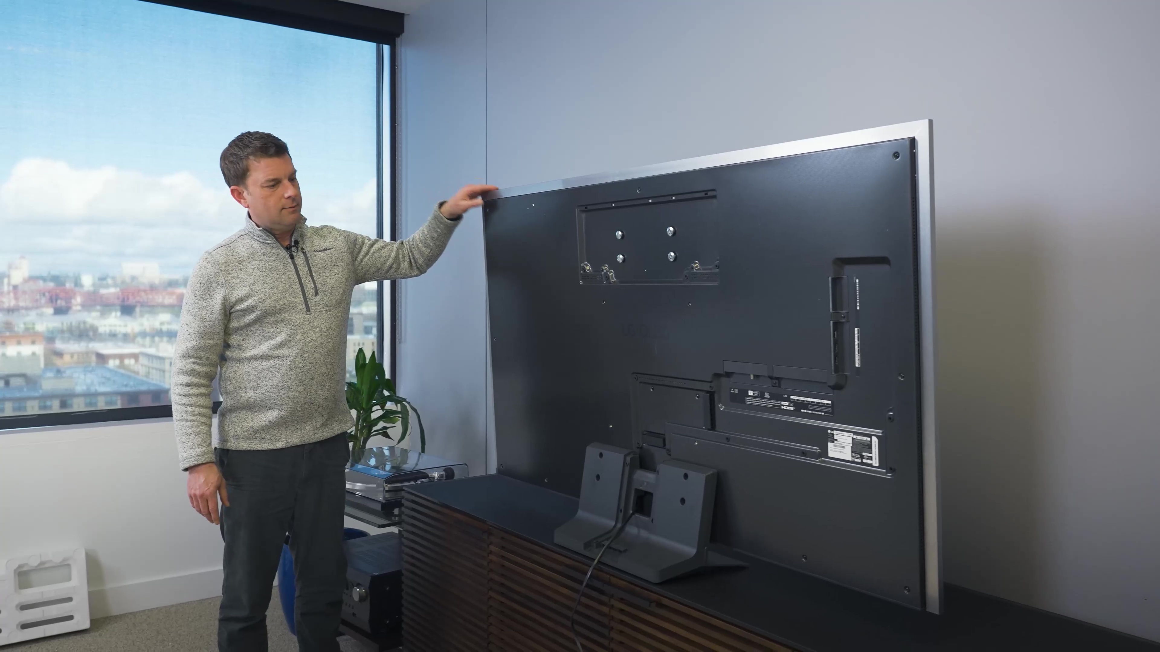 A man standing next to an LG G3 showing it's rear panel and stand.