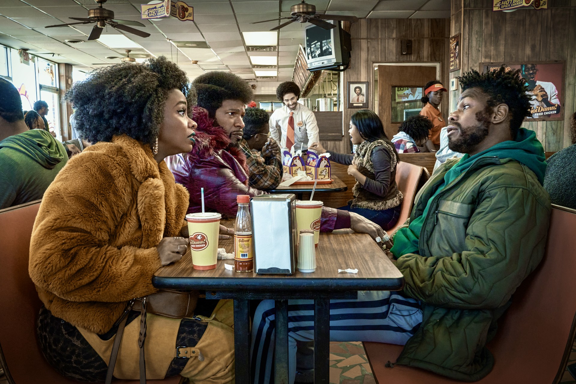 Three people sit at a table in They Cloned Tyrone.