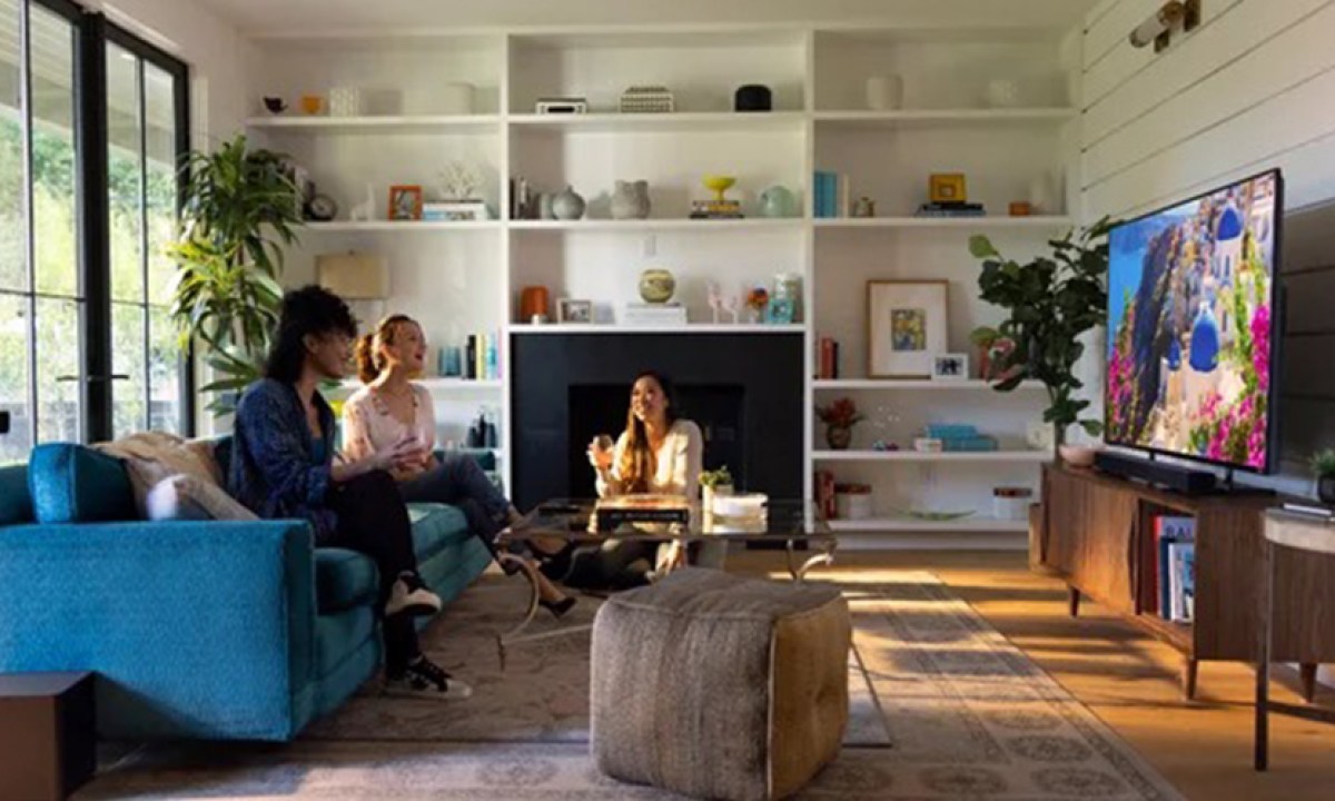 A living room with two people watching TV with the Vizio V-Series 2.1 Home Theater Soundbar and subwoofer underneath.