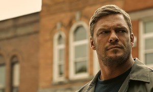 Alan Ritchson as Jack Reacher from the Amazon Prime Video series Reacher standing outside, looking menacing.