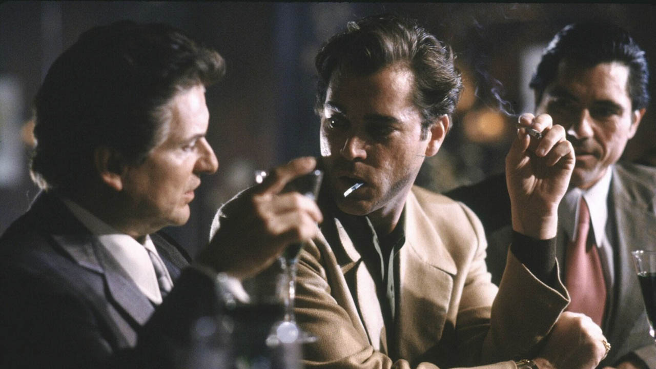 Three men sitting at a bar drinking and smoking in a scene from Goodfellas.