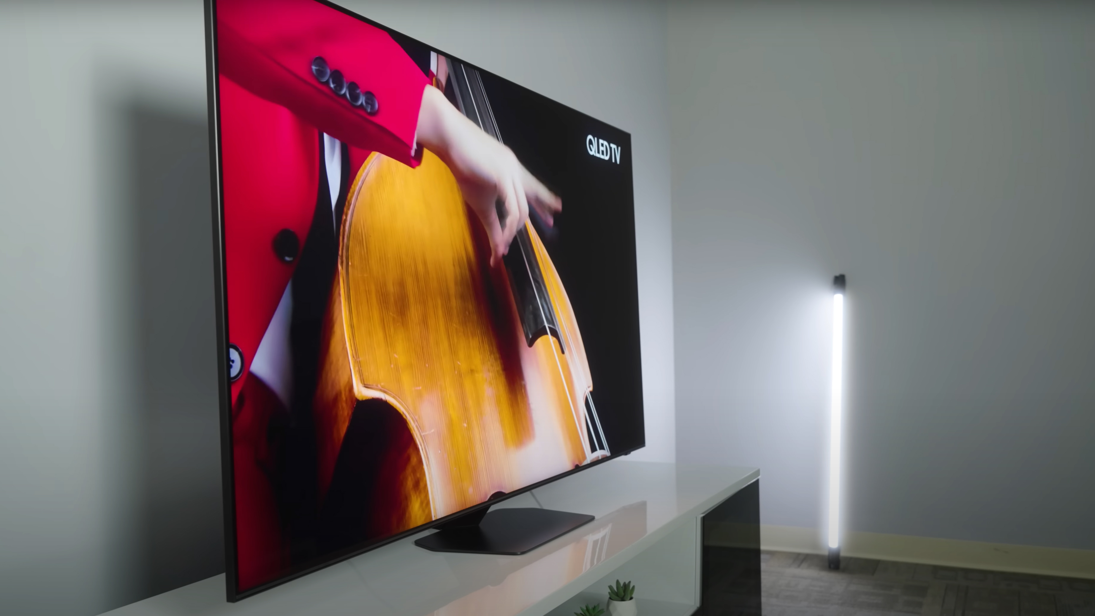 A closeup of a performer in a red jacket plucking an upright bass shown on a Samsung QN90D TV.