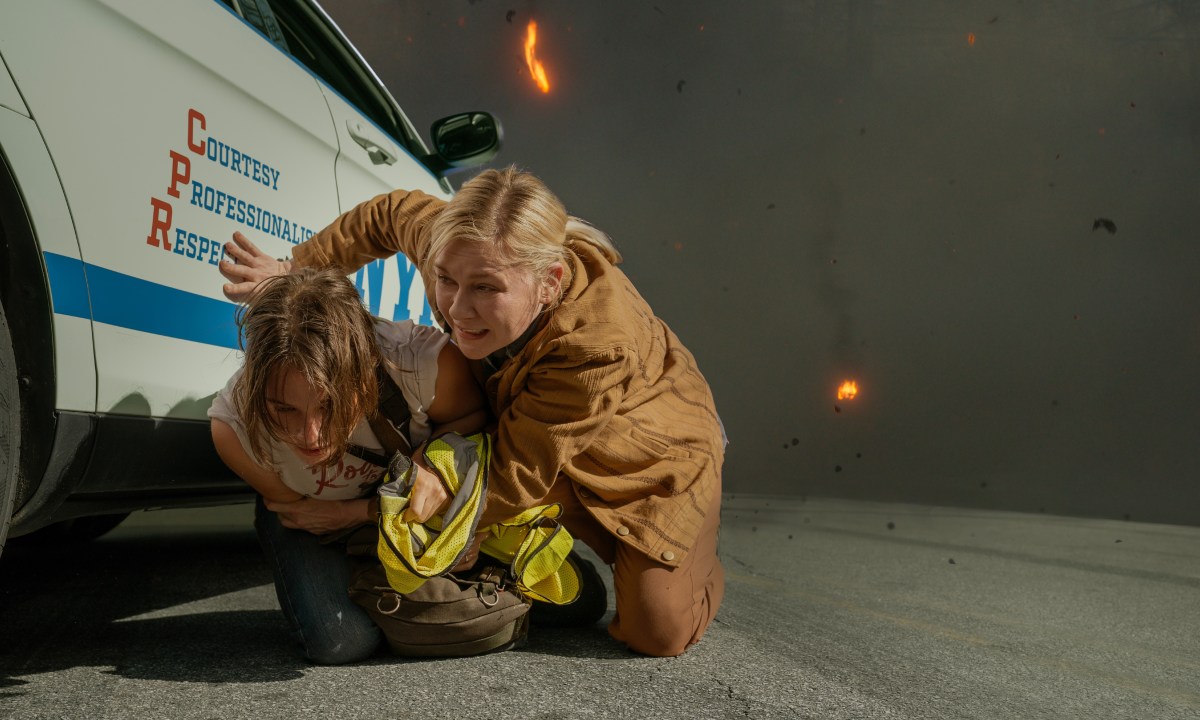 Cailee Spaeny and Kirsten Dunst crouch next to a car in Civil War.