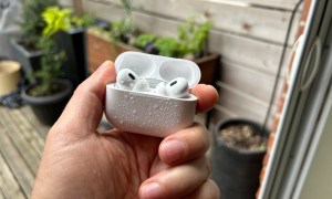 A pair of Apple AirPods Pro in an open case with water splashed on them.
