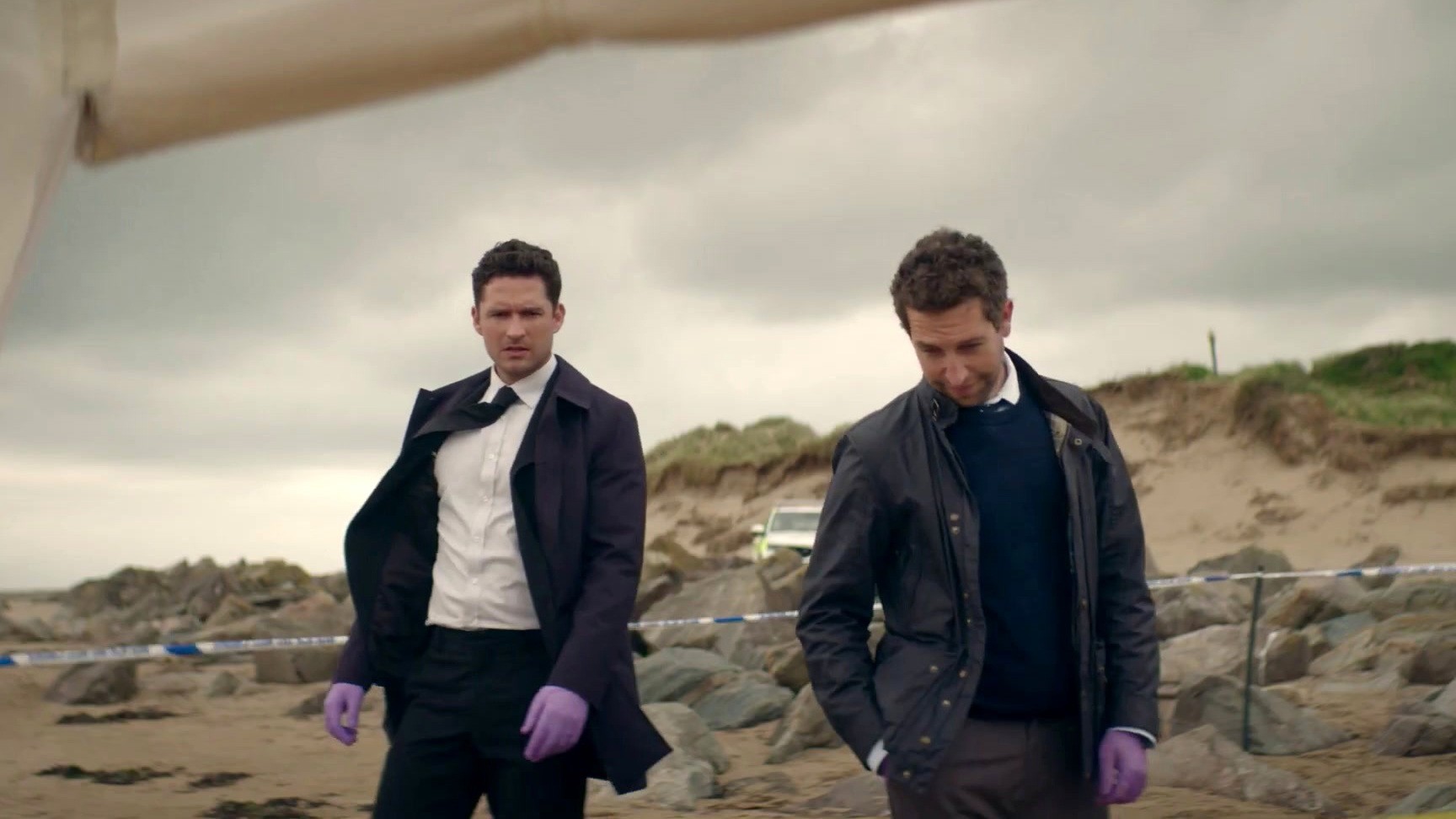 Two men stand on a beach in The Long Call.