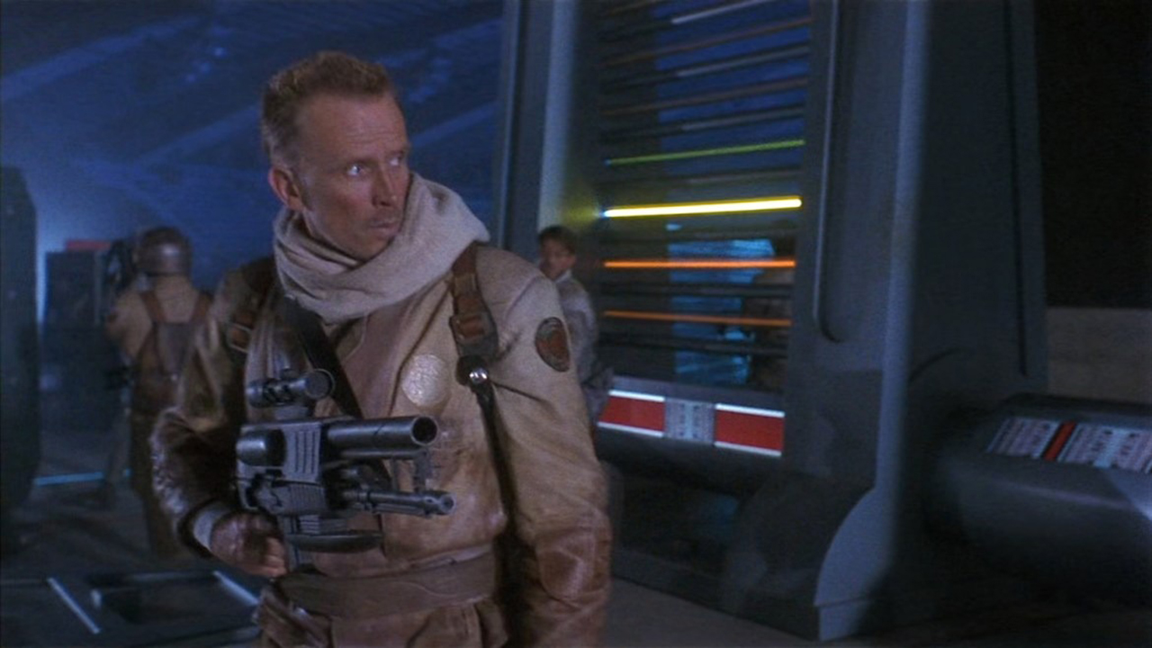 A man holding a gun and looking to the right in a scene from Screamers.