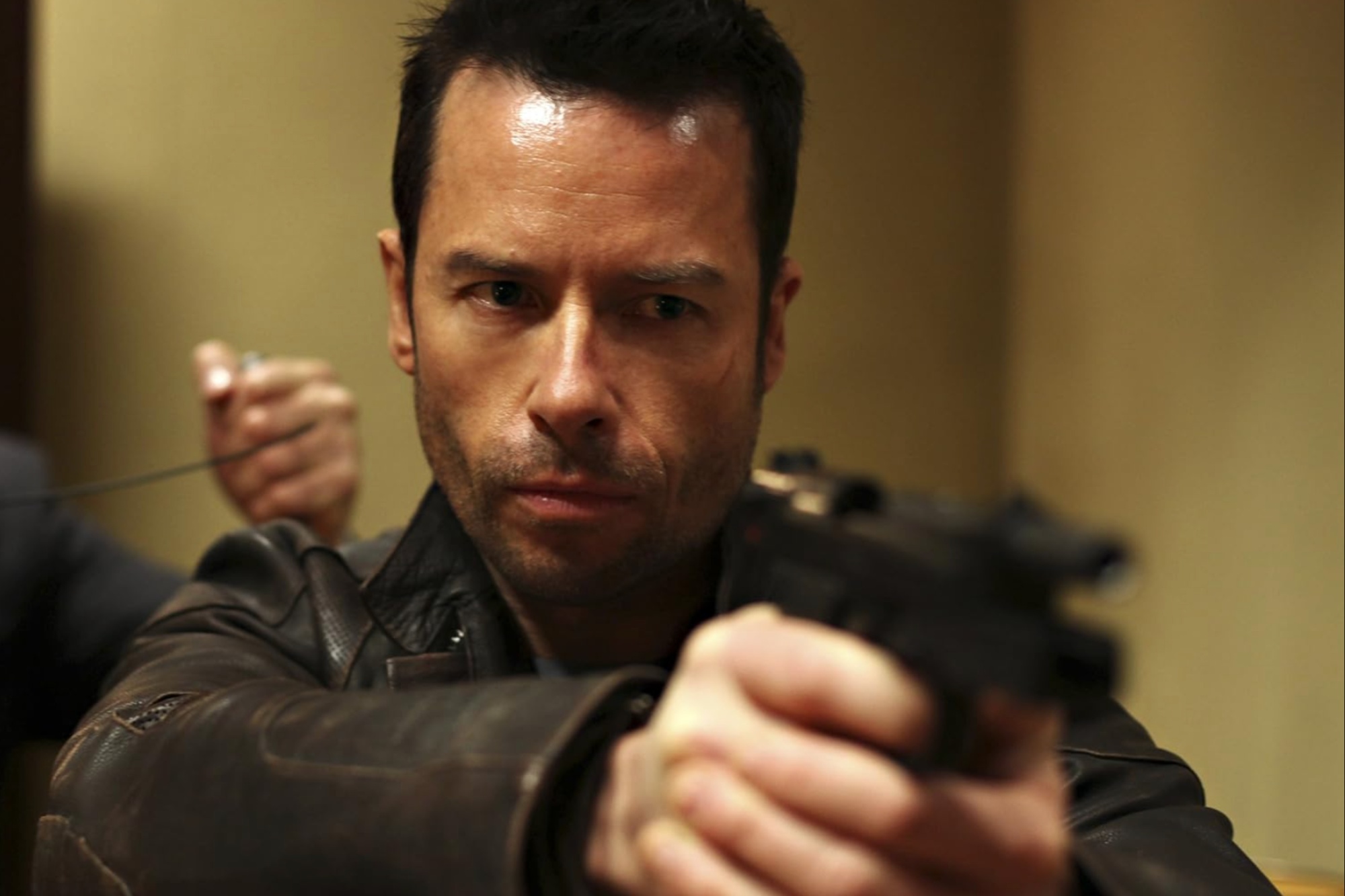 Guy Pearce holds and points a gun.