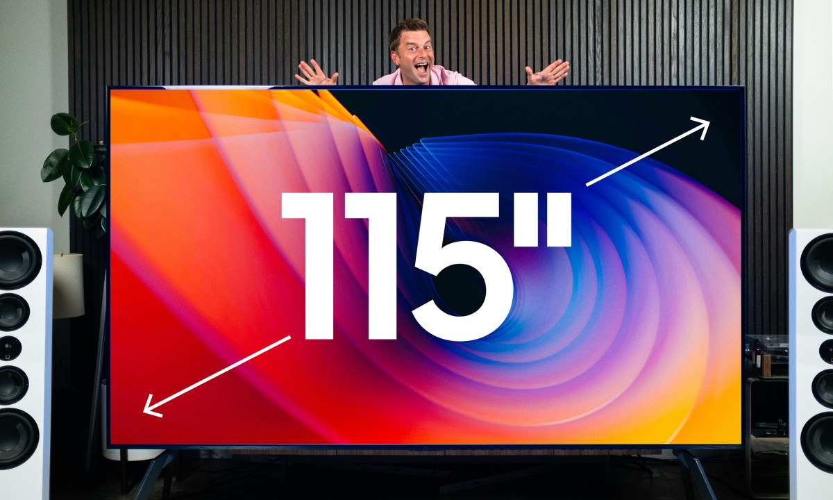 Caleb Denison stands behind a 115-inch TCL QM89 4K TV.