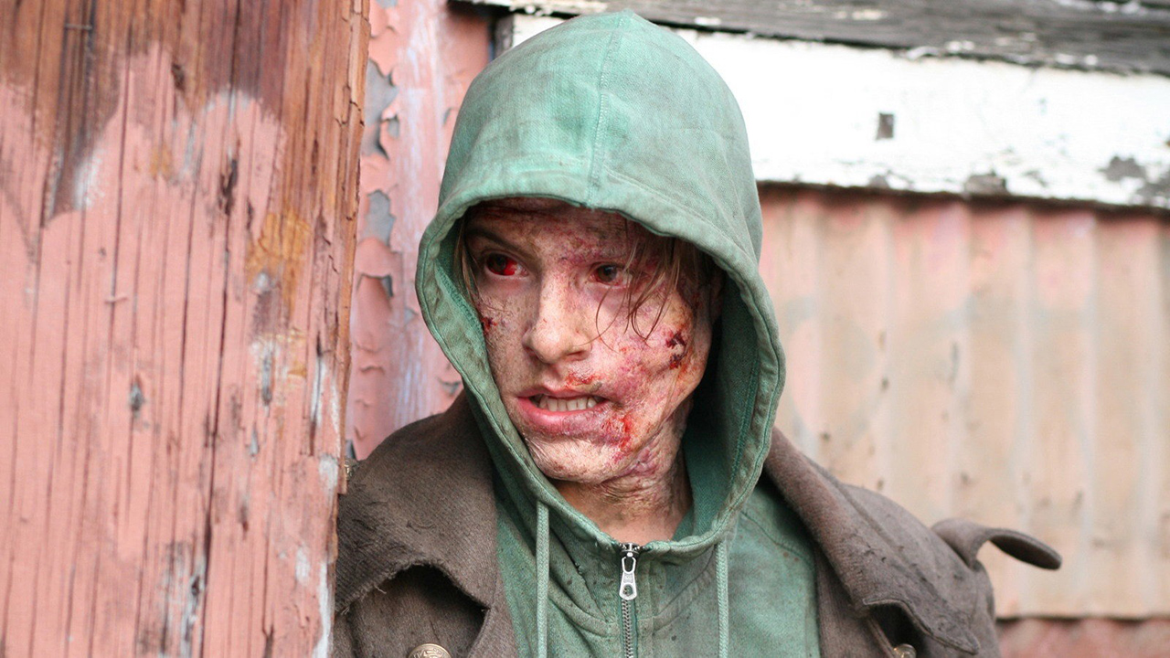 A disfigured man wearing a green hoodie with blood on his face in Frankenstein.