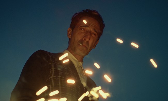 Adrien Brody smokes as sparks dance around him in a still from the movie The Brutalist