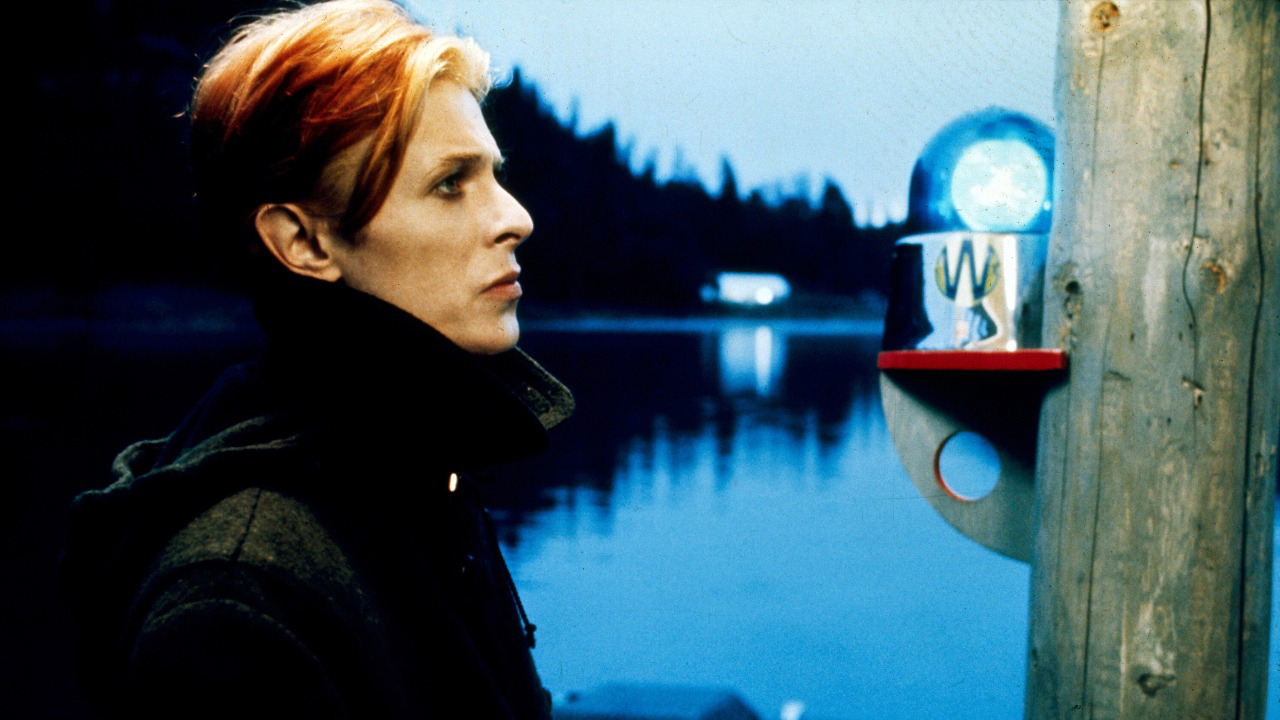 A side profile of David Bowie in a black jacket standing by the water in The Man Who Fell To Earth.