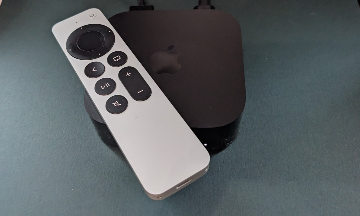 An Apple TV 4K sits against a green background. The silver apple remote sits on top of the streaming box.