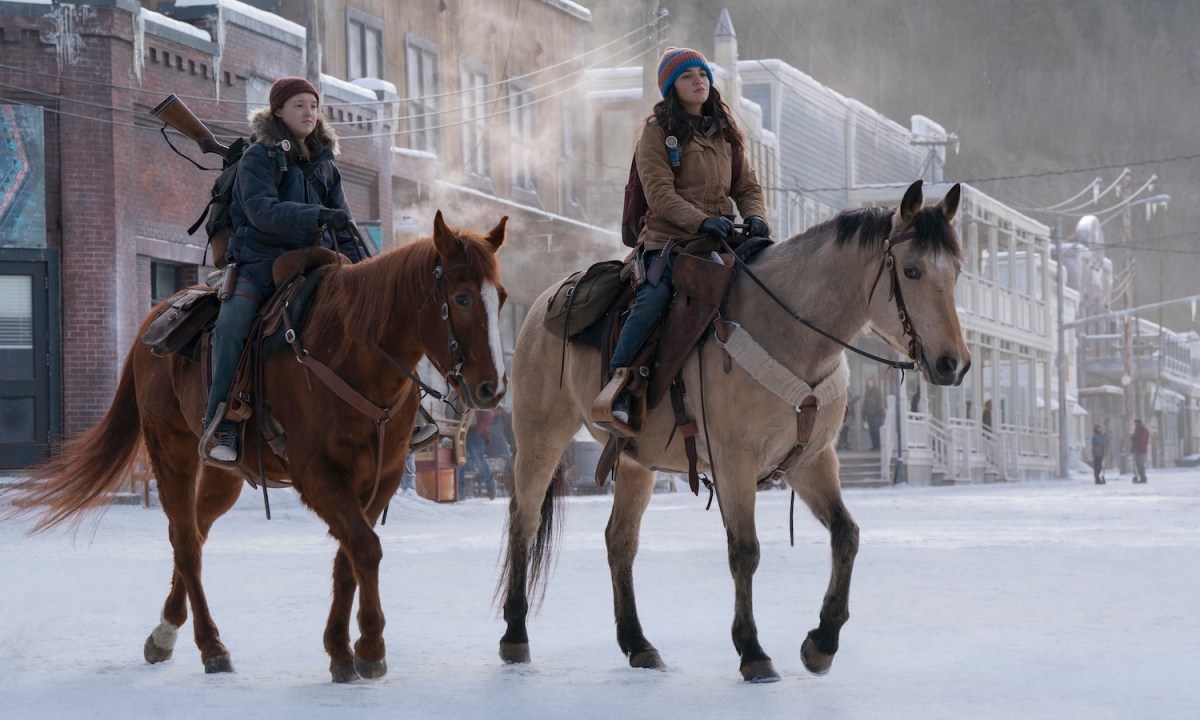 Two girls on horses trot in the snow.