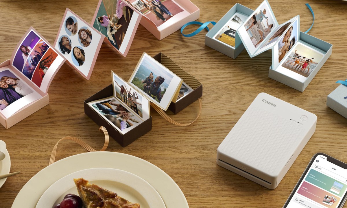 Canon's Selphy QX20 rests on a table beside a phone and photo albums.
