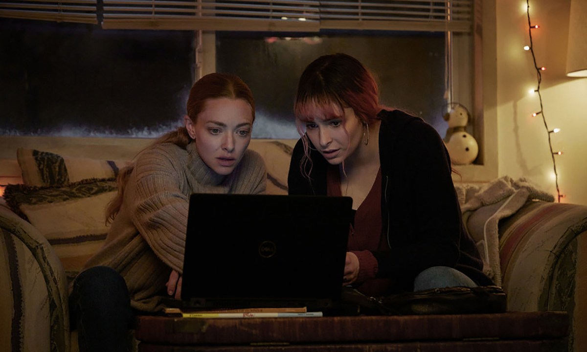 Two women sit on a couch in the dark looking at a computer screen and pointing in Long Bright River.