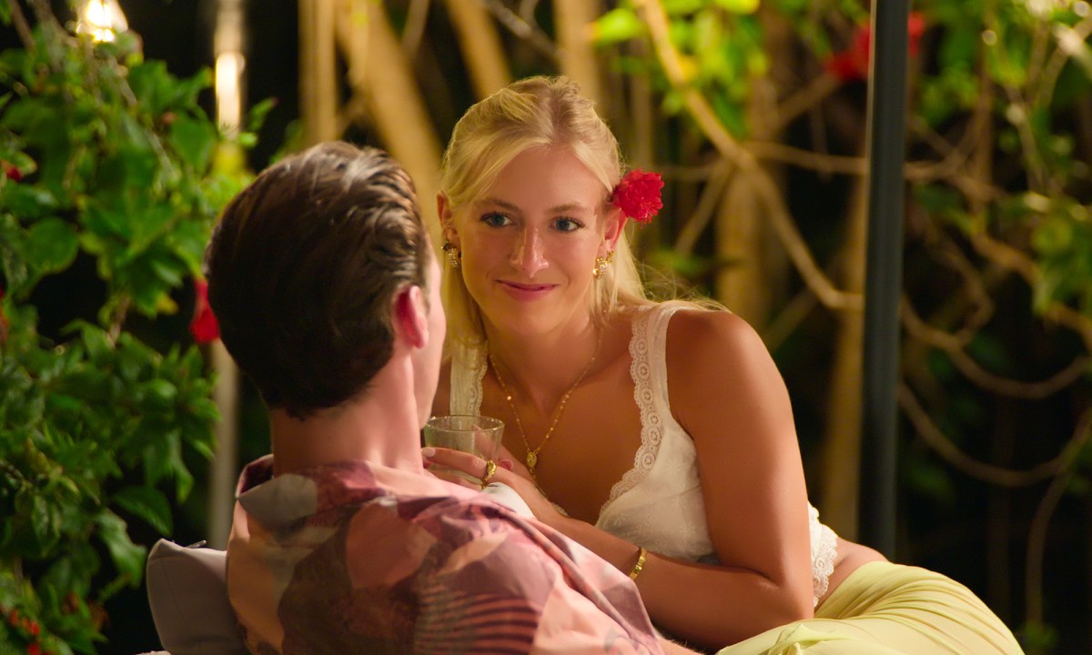 A young, blonde woman with a flower in her hair smiles while talking to a young man in Temptation Island.